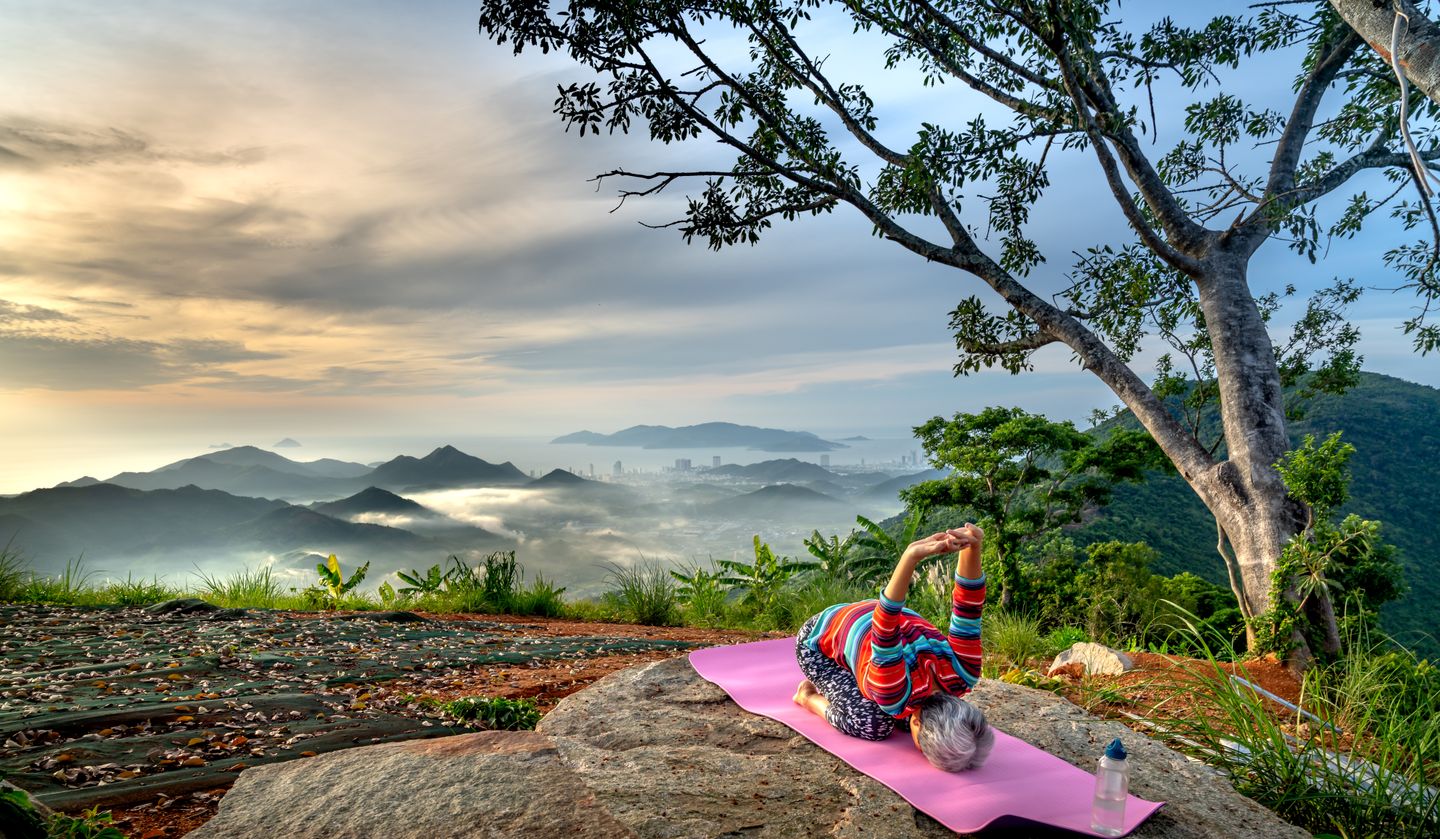 Elderly woman performing yoga on a mountain with a breathtaking view, promoting active and healthy lifestyle.